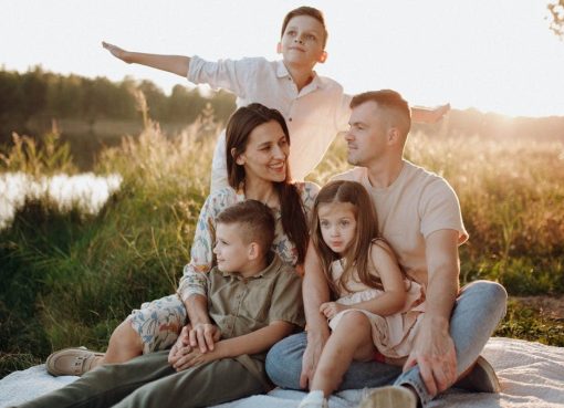 A family of five enjoying a serene picnic in a sunlit meadow during sunset.